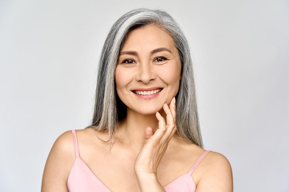 Smiling woman with gray hair touching her face, promoting Xeomin treatment.